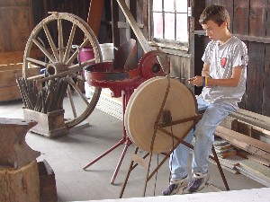 A young apprentice demonstrates use of the old pedal grinder.